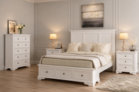 White wooden bedroom furniture set including a bed frame with storage drawers, a tall dresser, and two nightstands, styled in a neutral bedroom with beige walls, wood floors, and matching lamps.