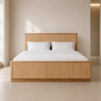 A modern platform bed with a light natural wood slatted headboard and footboard, dressed in white bedding and pillows, set against a minimalist beige wall and floor.