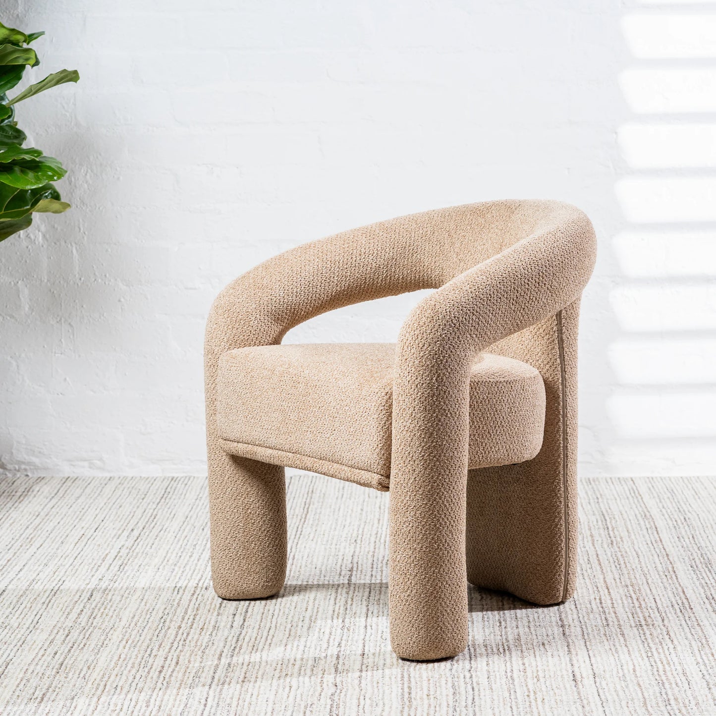 A modern low-profile armchair upholstered in a textured beige bouclé fabric