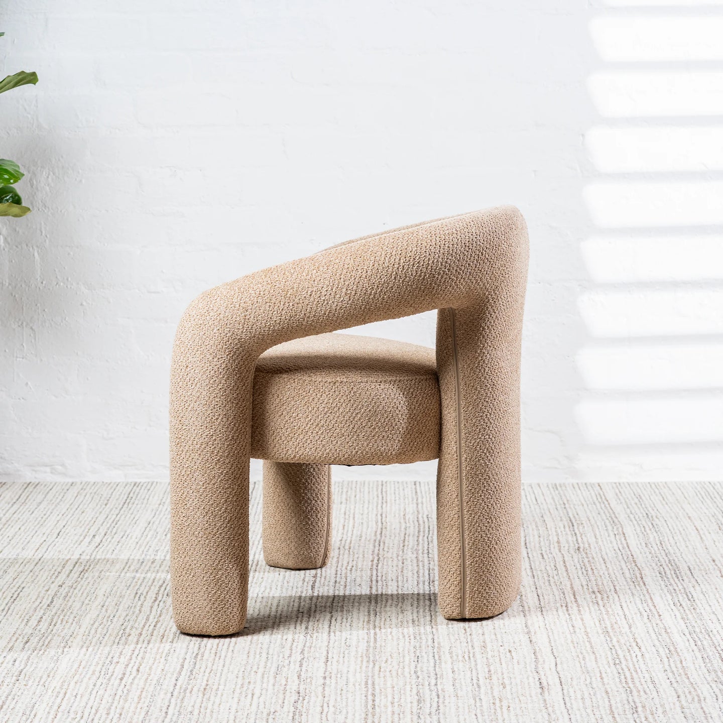 A modern upholstered accent chair with a chunky curved backrest and cylindrical legs, upholstered in a textured beige fabric