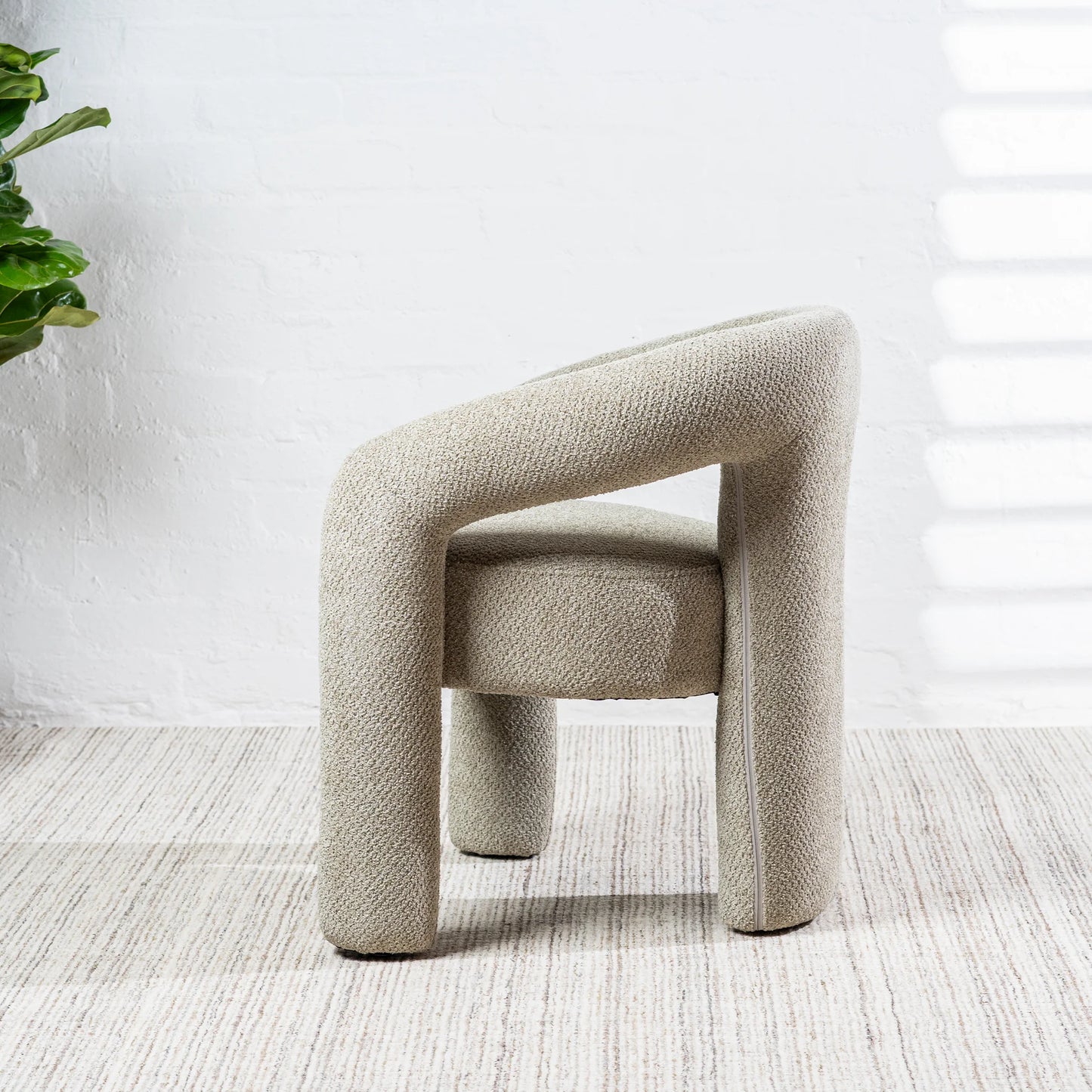 A modern upholstered accent chair with a chunky curved armrest and thick legs, upholstered in a textured light beige fabric