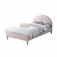 A single bed with a pale blush pink upholstered frame and a curved headboard, shown on a clean white background. The bed is styled with white bedding, a light gray throw blanket, and a round cream pillow.