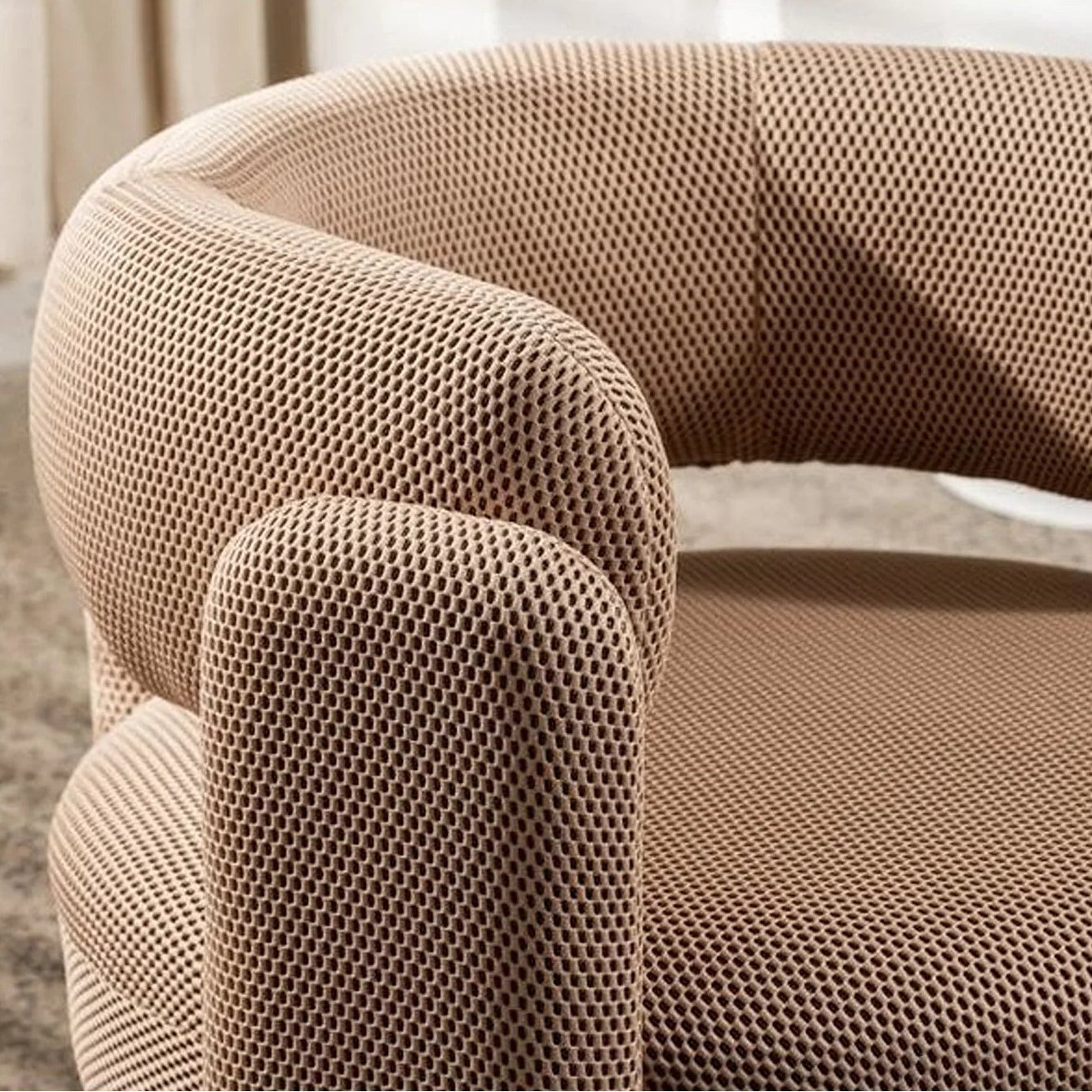 A close-up of a modern barrel-style armchair upholstered in a textured, woven beige fabric with a curved back and rounded arms.