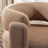 A close-up of a modern barrel-style armchair upholstered in a textured, woven beige fabric with a curved back and rounded arms.