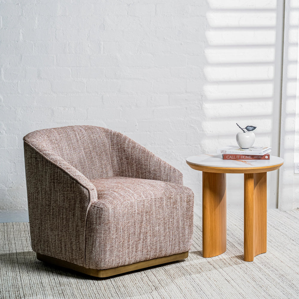A modern barrel-style armchair in textured taupe upholstery sits beside a small round side table with a white top and light wood legs