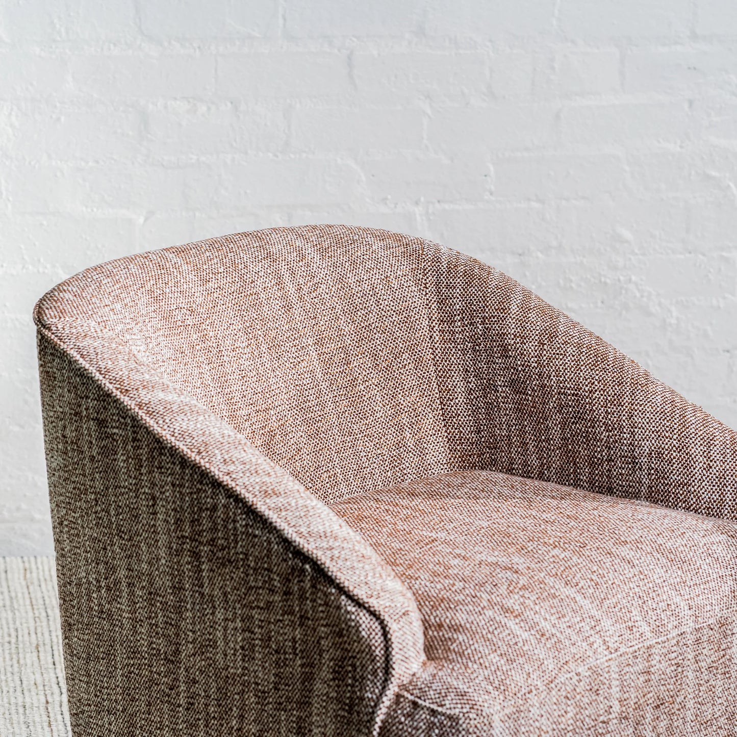 A close-up of a modern barrel-style armchair upholstered in a textured herringbone fabric in warm taupe and brown tones