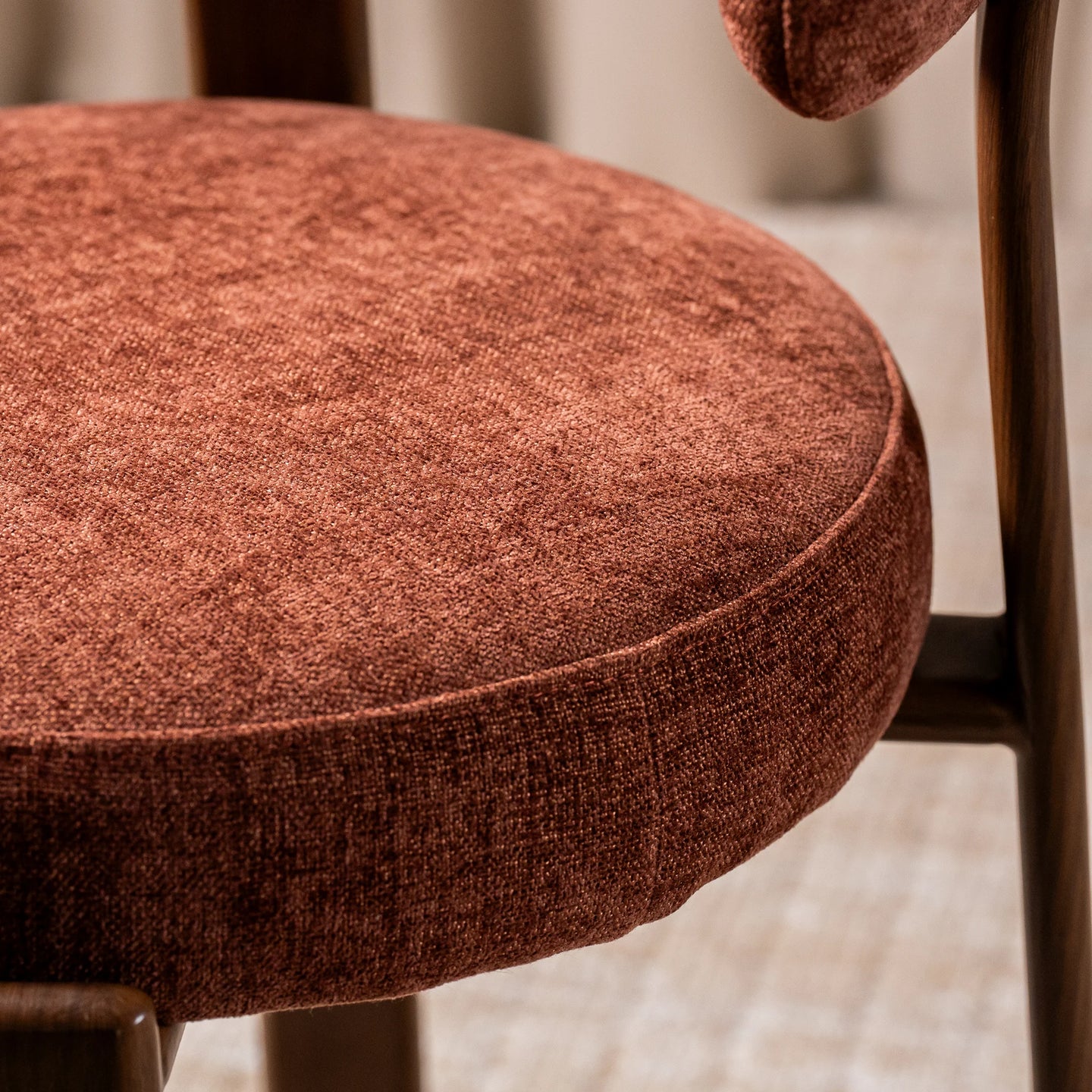 Close-up of a round upholstered chair cushion in a textured rust-brown fabric, showing the seat and part of the backrest on a wooden chair.