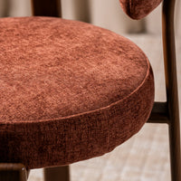 Close-up of a round upholstered chair cushion in a textured rust-brown fabric, showing the seat and part of the backrest on a wooden chair.