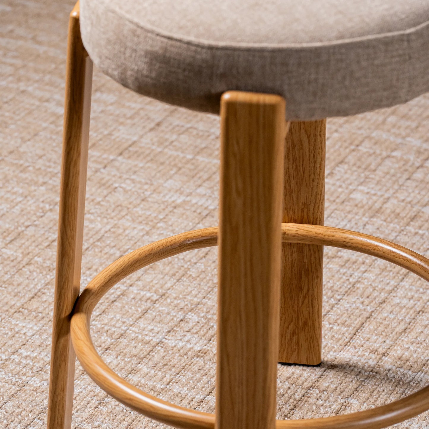 Close-up of a bar stool with a round upholstered seat in light beige fabric and a curved wooden footrest