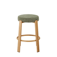 A modern bar stool with a round, textured sage green upholstered seat and four light natural wood legs, featuring a lower circular footrest ring.