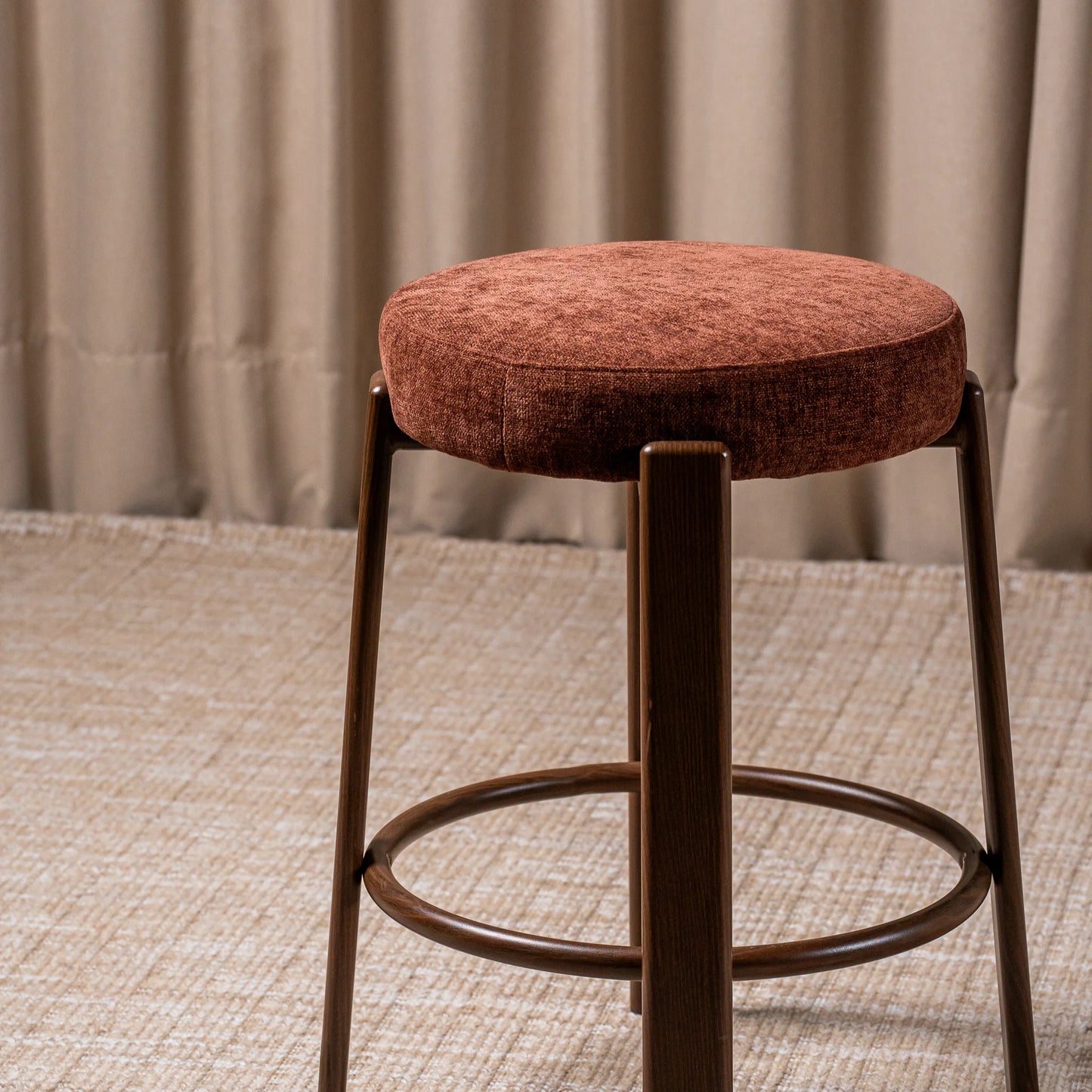 A round bar stool with a textured rust-brown upholstered cushion and a dark brown wooden frame