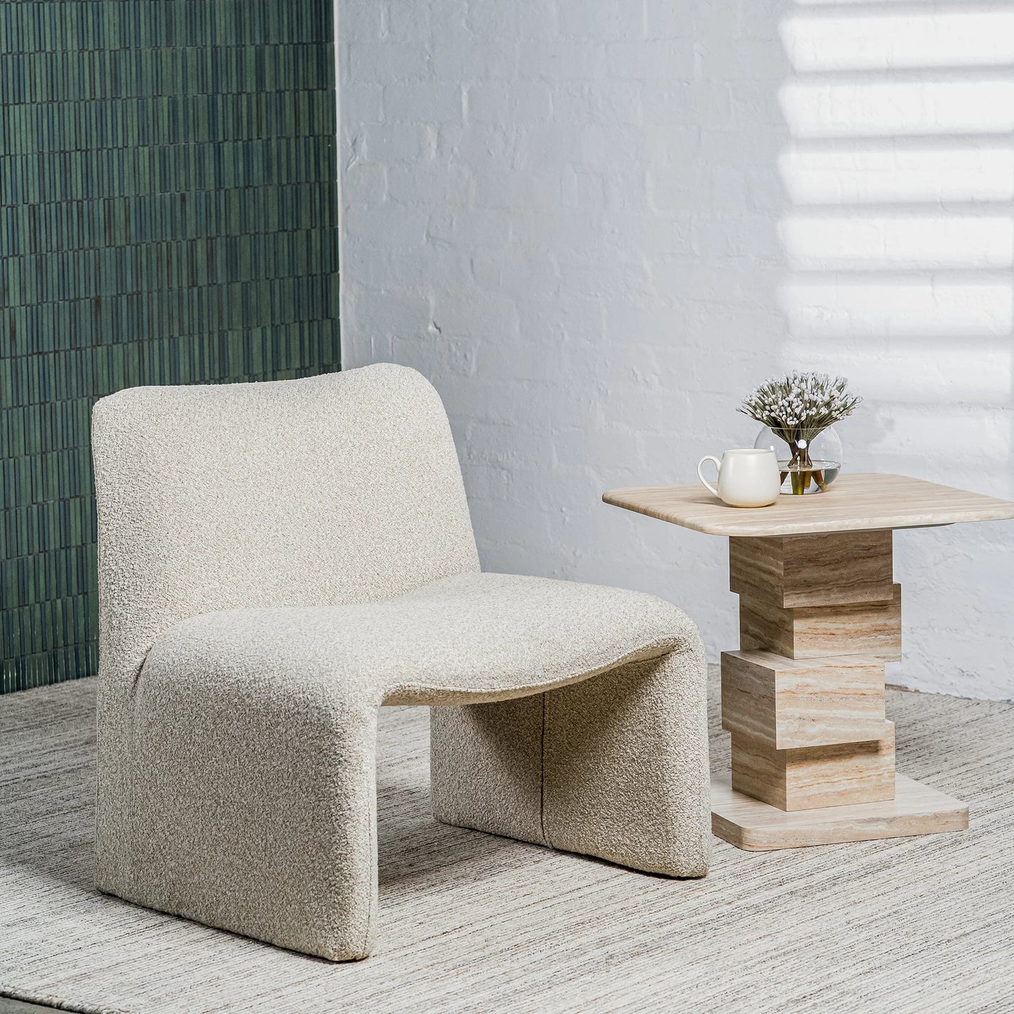 A modern upholstered accent chair in textured cream bouclé fabric sits beside a light wood side table with a small vase in a styled interior setting.