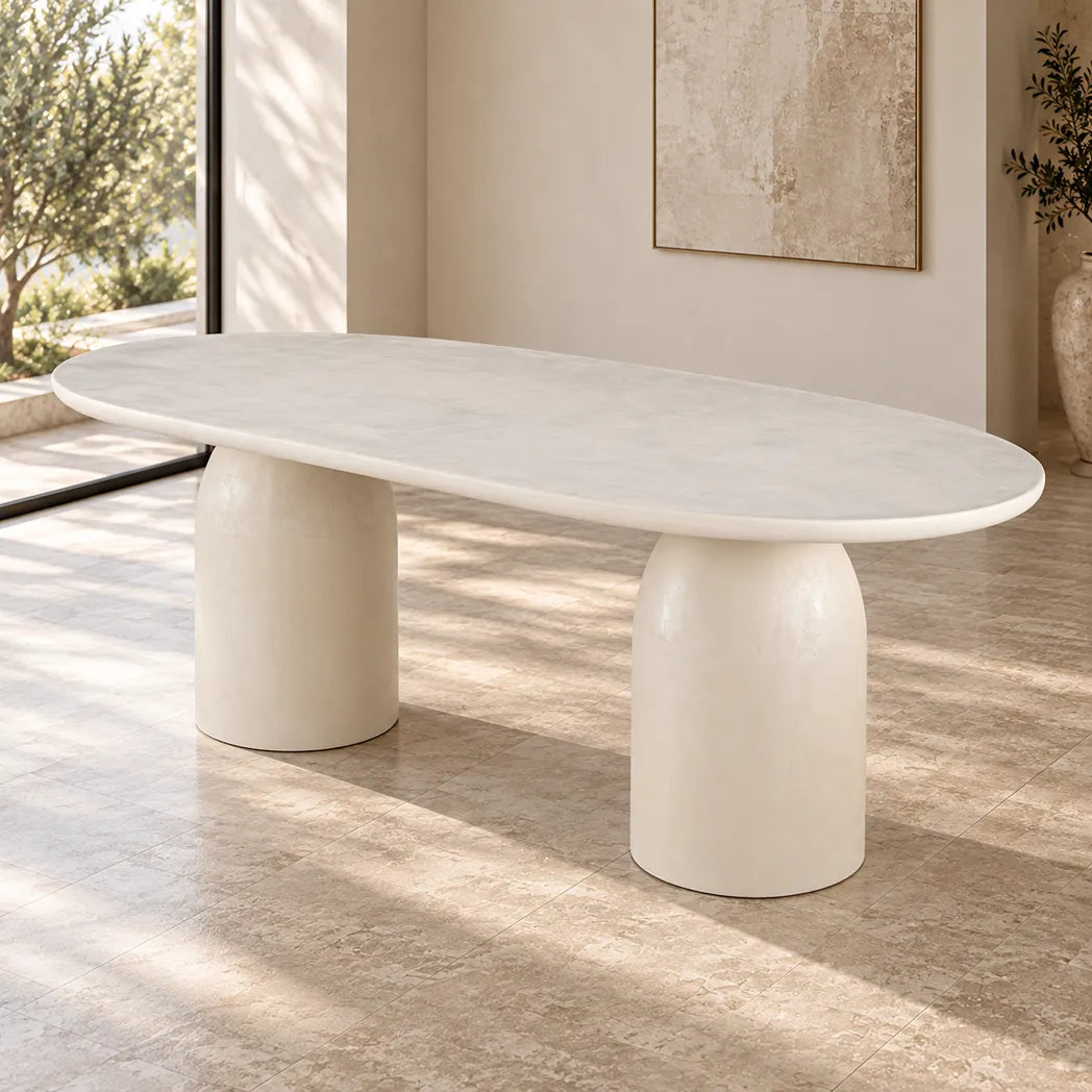 Calisto Pebble oval dining table with micro-cement finish and two cylindrical pedestal bases, angled front view