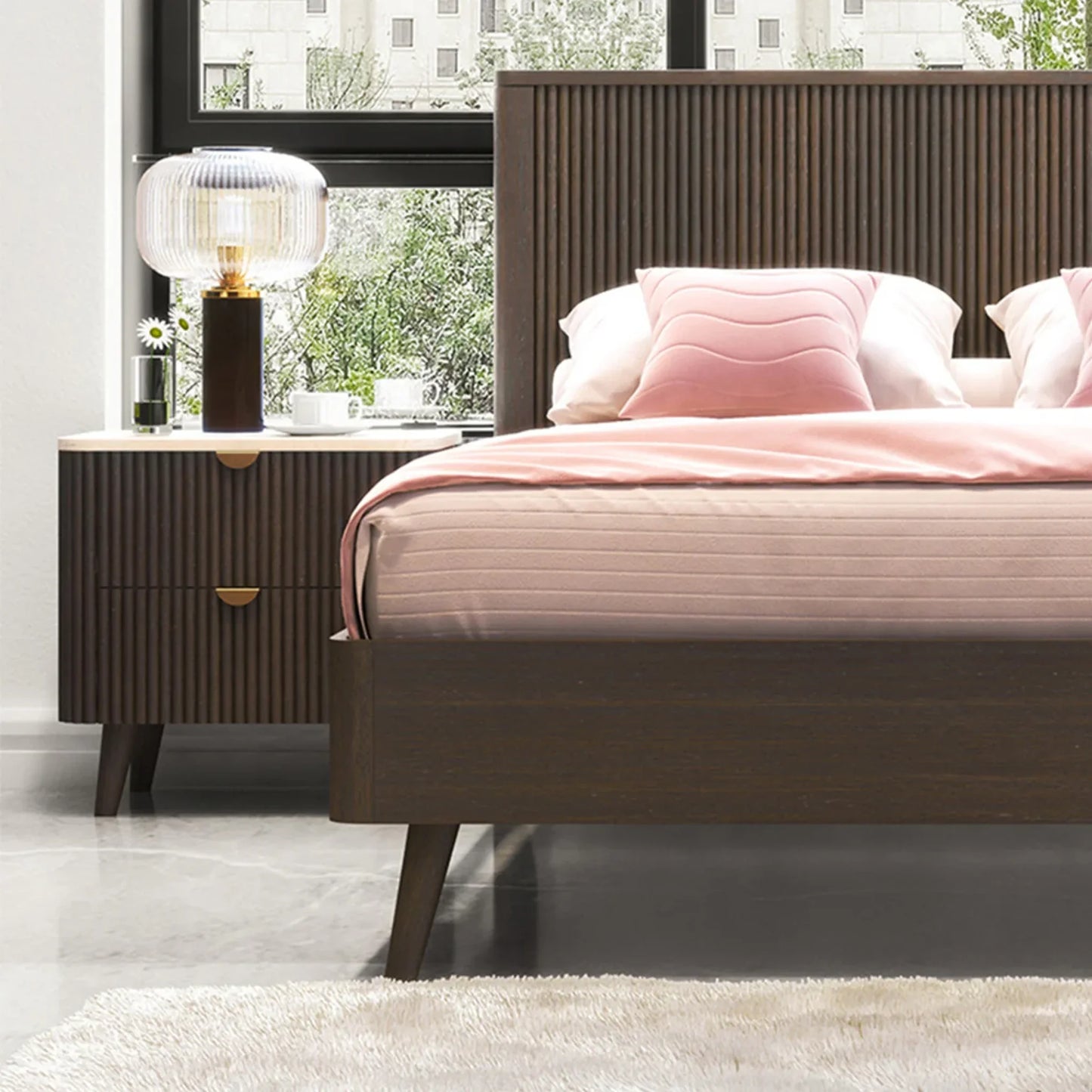 A modern bedroom scene featuring a dark brown wooden bed frame with a slatted headboard, dressed in pink bedding and pillows, next to a matching dark brown nightstand with a ribbed front and gold pull handles.