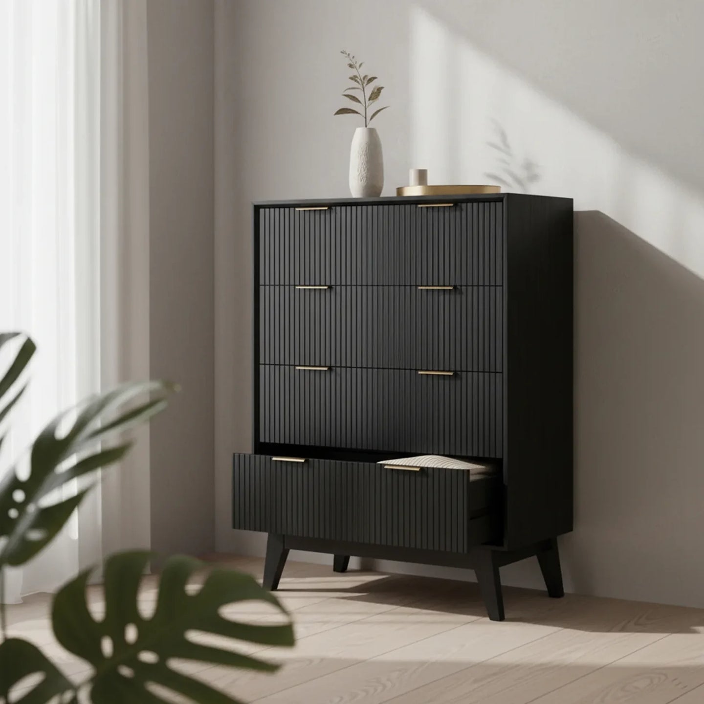 Black dresser with gold handles in a room with sunlight and plant leaves.