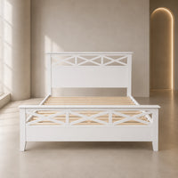 A white wooden bed frame with a headboard and footboard featuring decorative crisscross lattice panels, shown with light natural wood slats in a minimalist beige bedroom setting.
