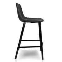 A modern counter stool with a black faux-leather upholstered seat and backrest, supported by a slim black metal frame with a footrest, shown from a side profile on a white background.