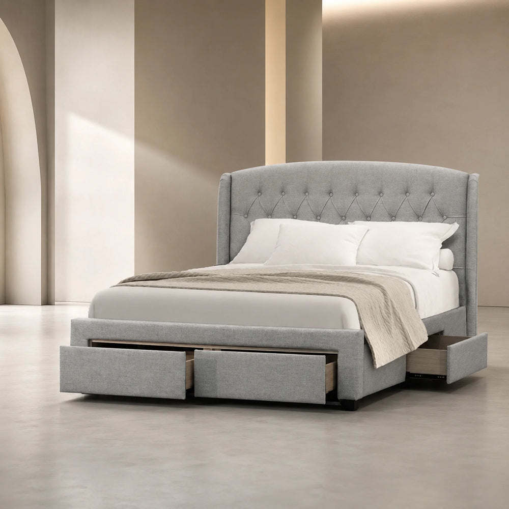 A modern platform bed with a tall tufted headboard and built-in storage drawers at the base, upholstered in light gray fabric and shown with white bedding in a minimalist beige-toned room.