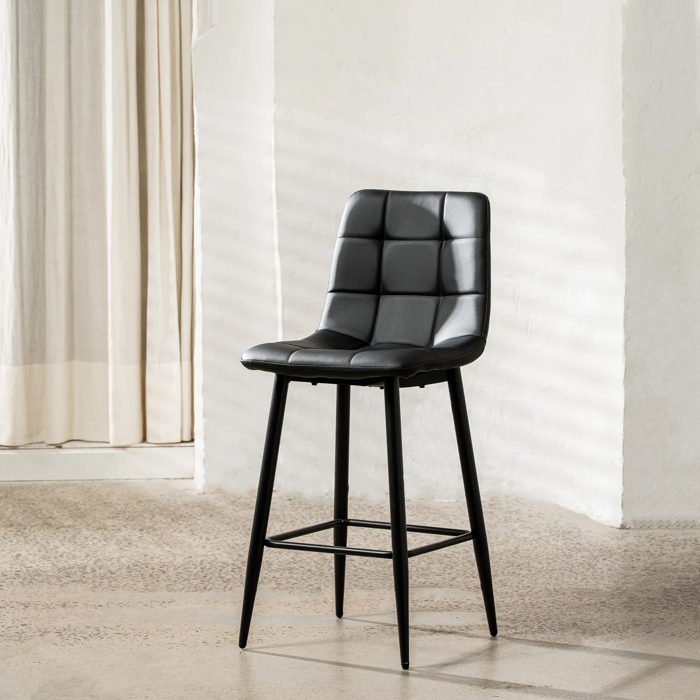 A black faux leather bar stool with a padded, tufted square backrest and four tapered legs