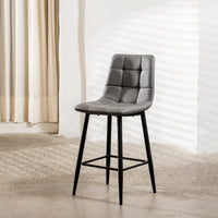 A modern gray upholstered bar stool with a padded segmented backrest, black metal legs, and a footrest