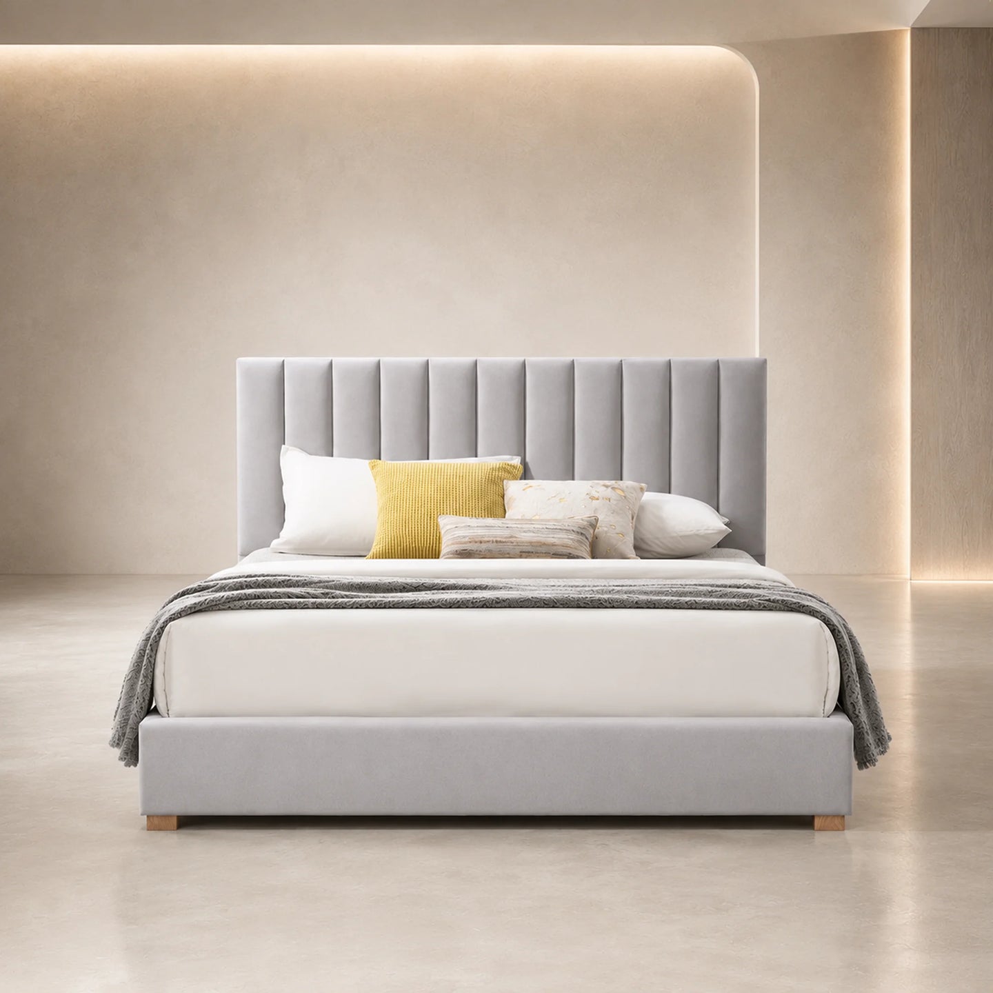 A modern gray upholstered bed with a tall channel-tufted headboard, styled with white and yellow pillows and a gray throw blanket, set in a minimalist beige room with warm ambient lighting.