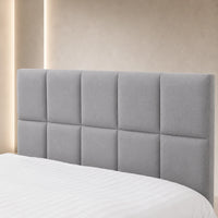 A light gray upholstered headboard with a tufted grid design, shown on a bed with white bedding against a warm beige wall with soft vertical lighting.