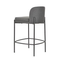 A modern gray upholstered bar stool with a dark metal frame and circular footrest, shown from a three-quarter angle on a white background.