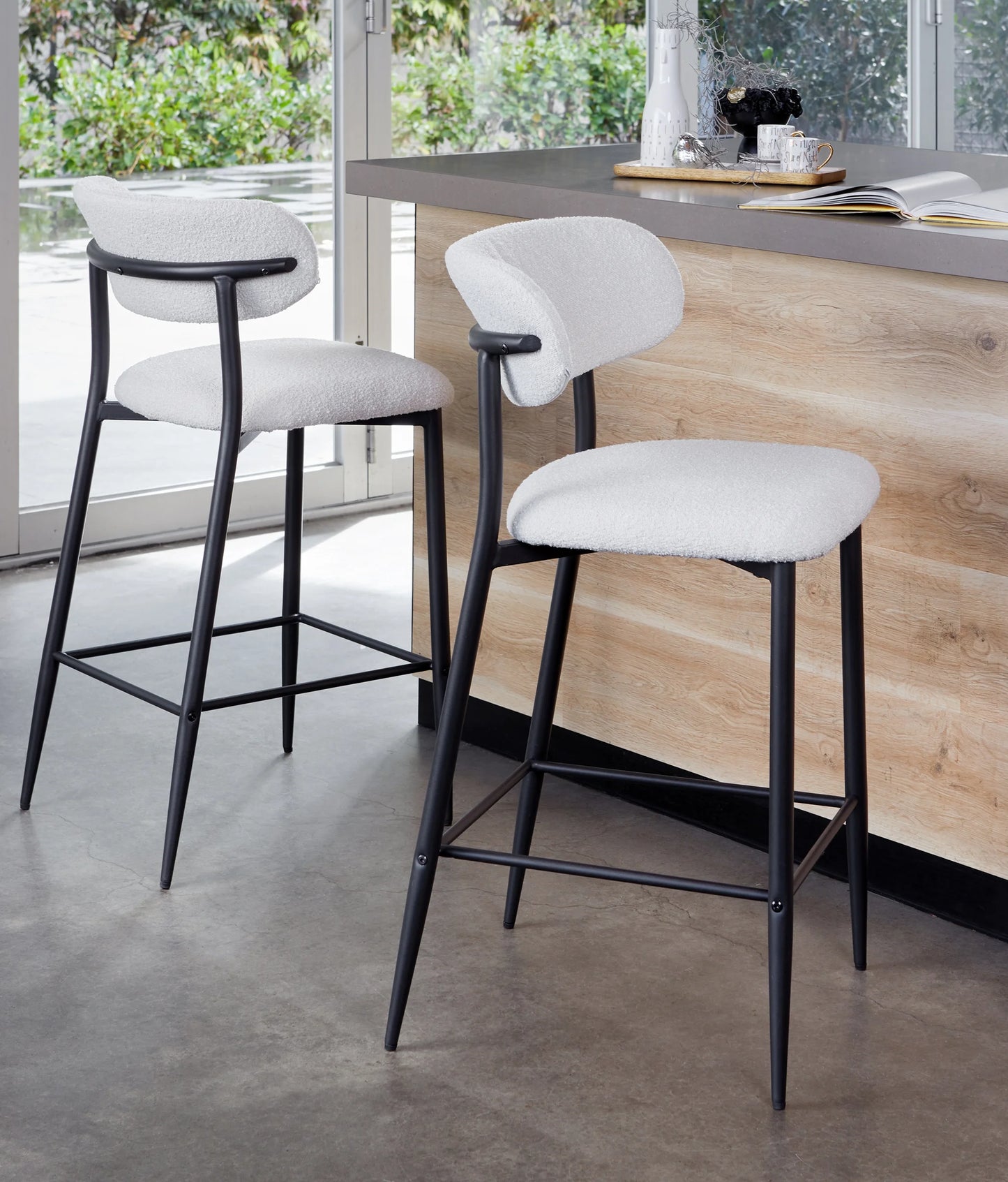Two modern bar stools with white textured upholstered seats and backs, black metal frames, and square footrests