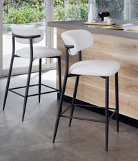 Two modern bar stools with white textured upholstered seats and backs, black metal frames, and square footrests
