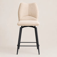 A modern bar stool with a curved, high-back upholstered seat in a textured cream fabric and a black metal frame with a footrest