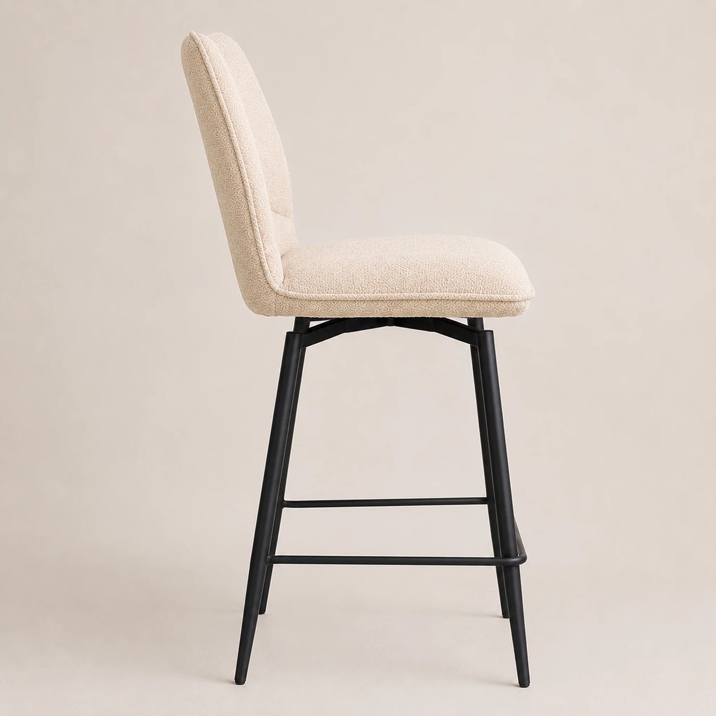 An upholstered bar stool with a cream-colored fabric seat and backrest, supported by a black metal swivel frame with a footrest