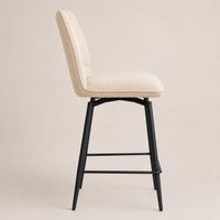 An upholstered bar stool with a cream-colored fabric seat and backrest, supported by a black metal swivel frame with a footrest