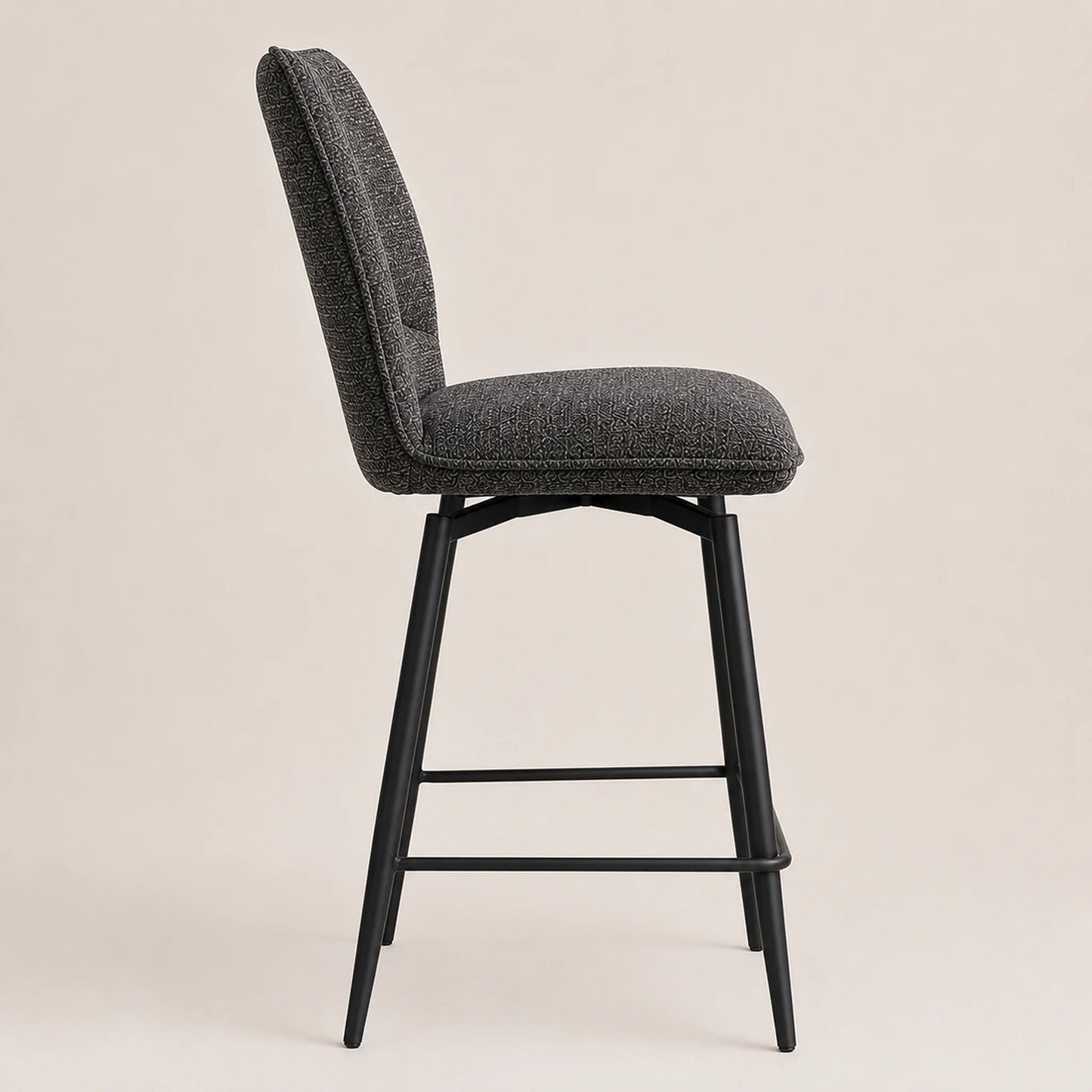 A modern bar stool with a textured dark gray upholstered seat and backrest, supported by a black metal frame with four legs and a footrest