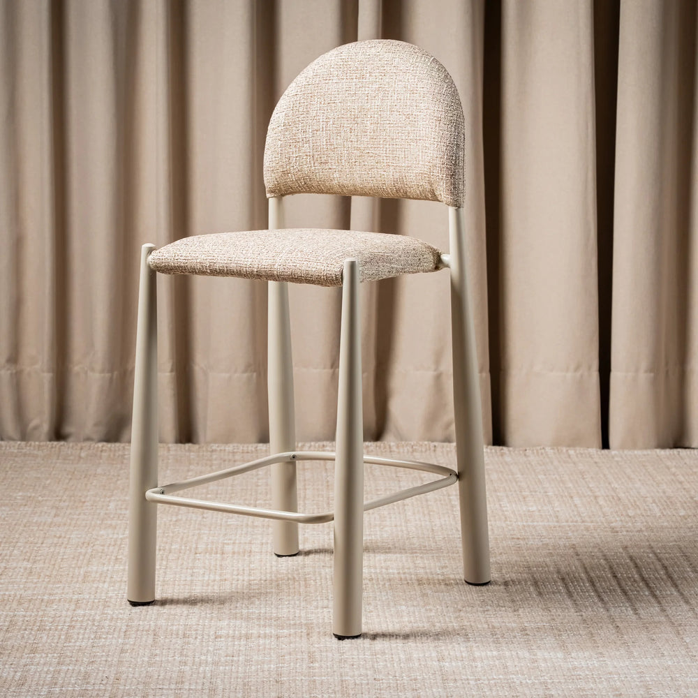 A modern bar stool with a light beige textured fabric seat and curved backrest, supported by a slim light gray metal frame with a footrest
