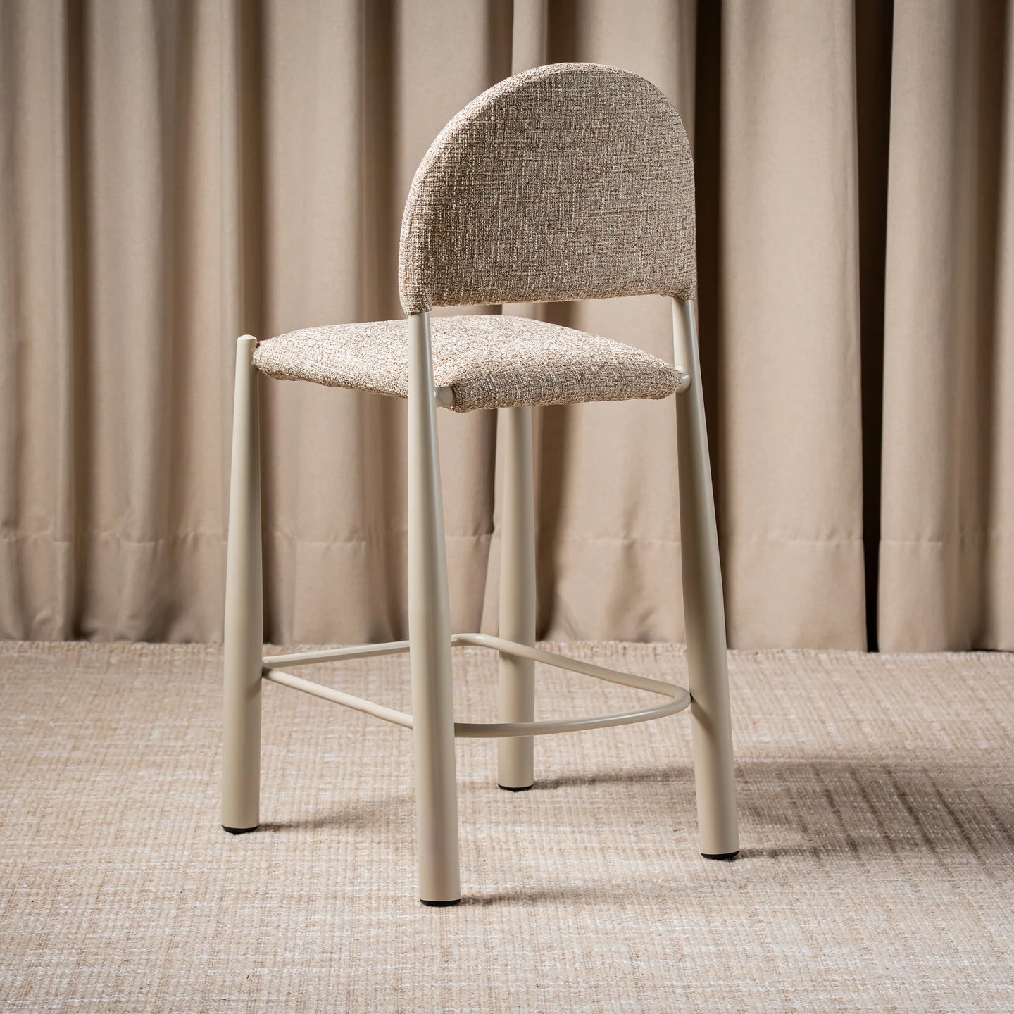 A modern counter stool with a textured beige upholstered seat and curved backrest, supported by slim light gray metal legs