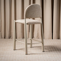 A modern counter stool with a textured beige upholstered seat and curved backrest, supported by slim light gray metal legs
