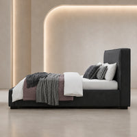 A modern platform bed with a tall upholstered headboard in dark charcoal gray, styled with white bedding, a textured gray throw blanket, and striped pillows, set against a minimalist beige wall with warm ambient lighting.