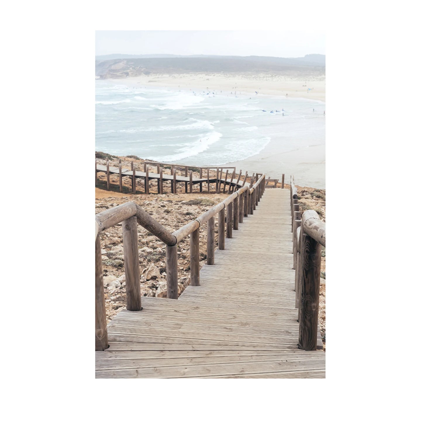 A wooden boardwalk leading down a sandy beach with ocean waves and distant dunes in the background.