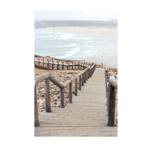 A wooden boardwalk leading down a sandy beach with ocean waves and distant dunes in the background.