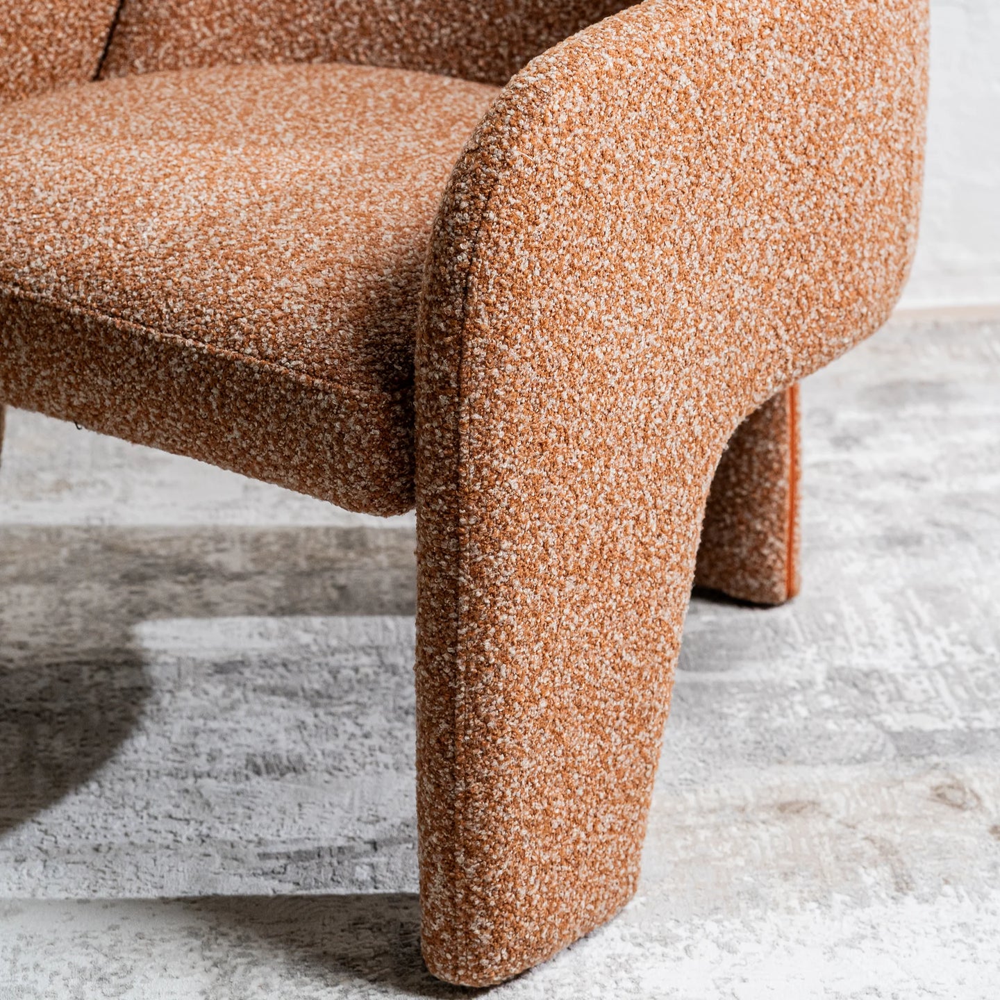 Close-up of a modern upholstered chair corner in a warm brown and beige textured fabric