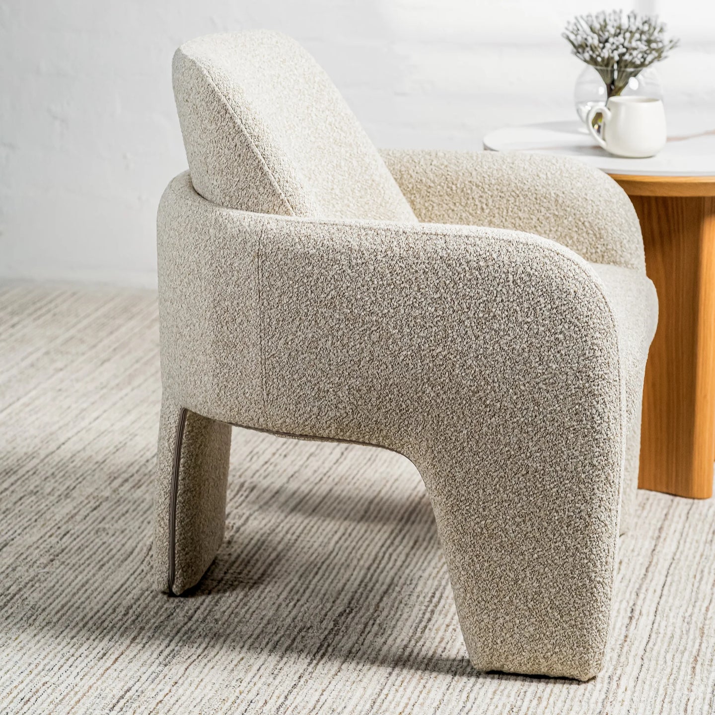 A modern sculptural armchair upholstered in a textured bouclé fabric in a light oatmeal beige color