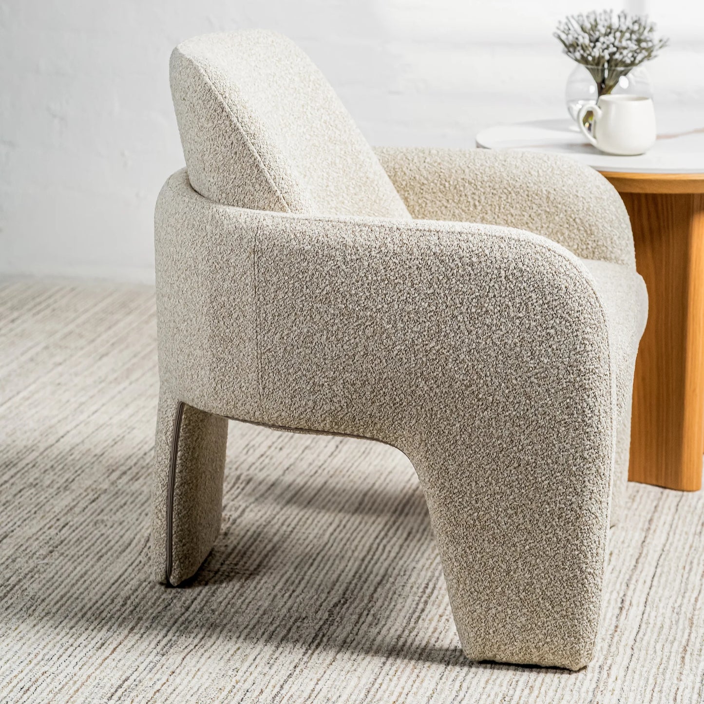 A modern sculptural armchair upholstered in a textured bouclé fabric in a light oatmeal beige color